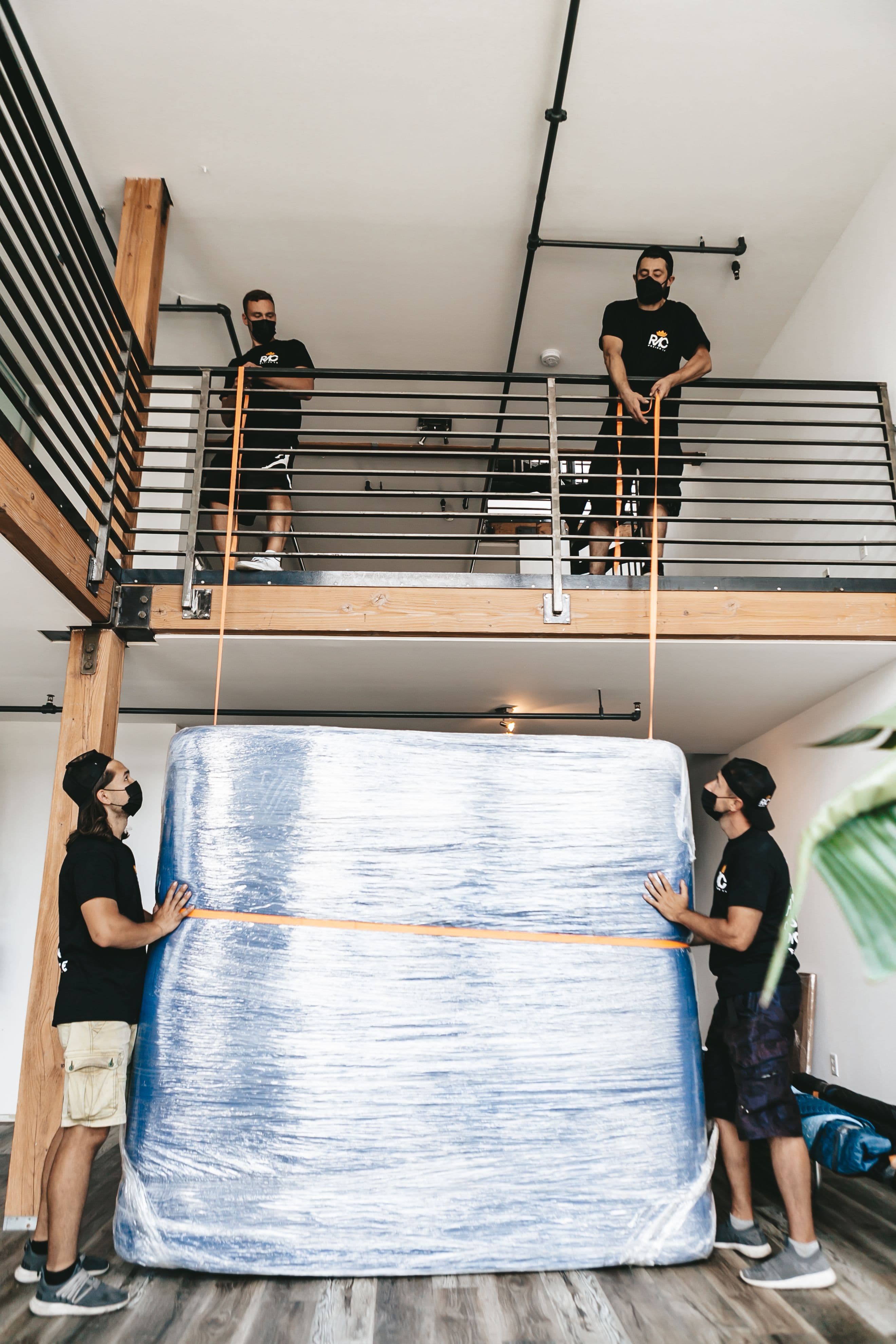 Movers using rigging straps to carefully lower a large wrapped item from a loft